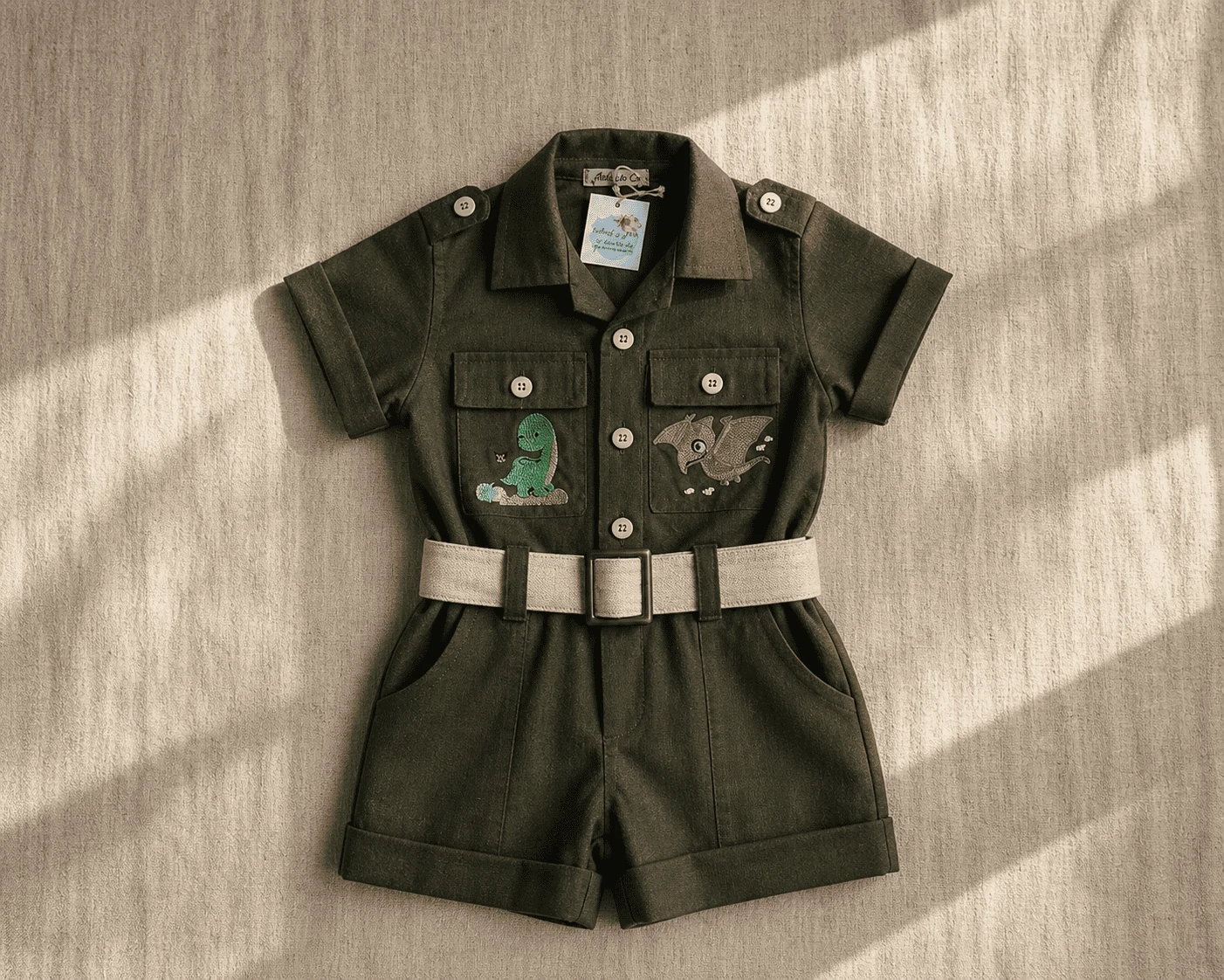 Macacão Safari Tema Dino · ensaio infantil expedição · paleta verde musgo · bordado temático personalizado · flat-lay editorial vintage
