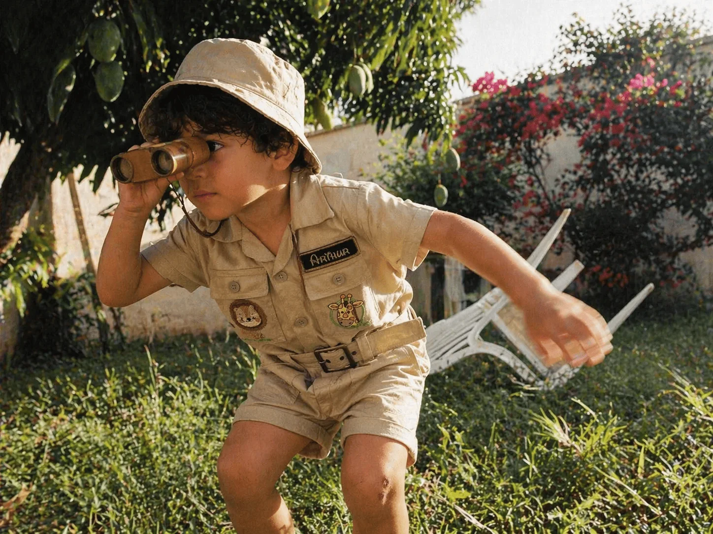 Menino no Macacão Safari brincando de aventura no quintal · cena de domingo de manhã, luz natural, peça vestida pelo cotidiano da criança