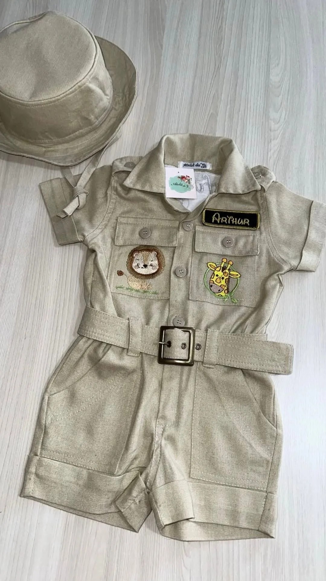Macacão Safari na cor bege com chapéu combinando, bordados de leão e girafa, etiqueta Arthur e cinto com fivela